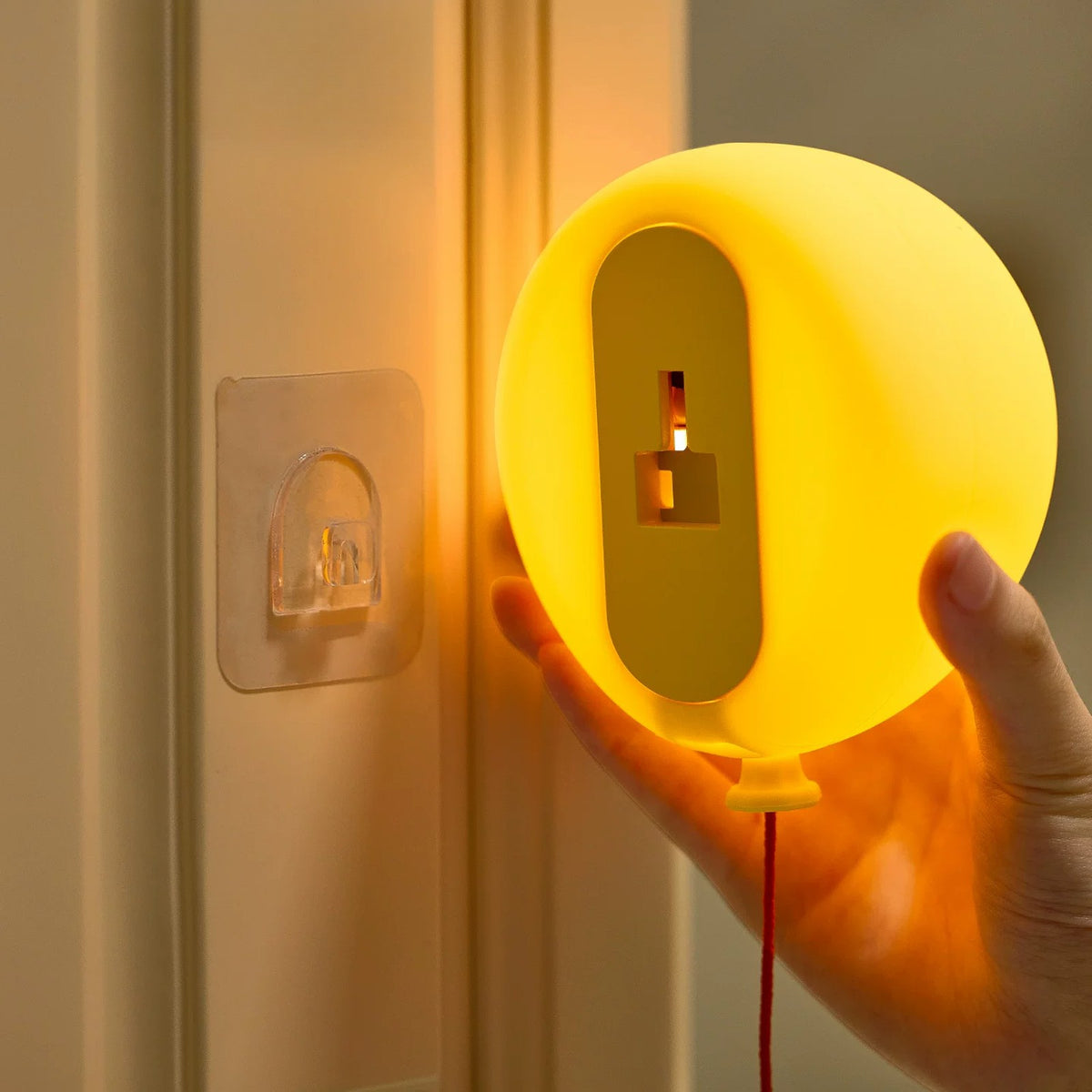 Hand holding the balloon light near its adhesive wall hook