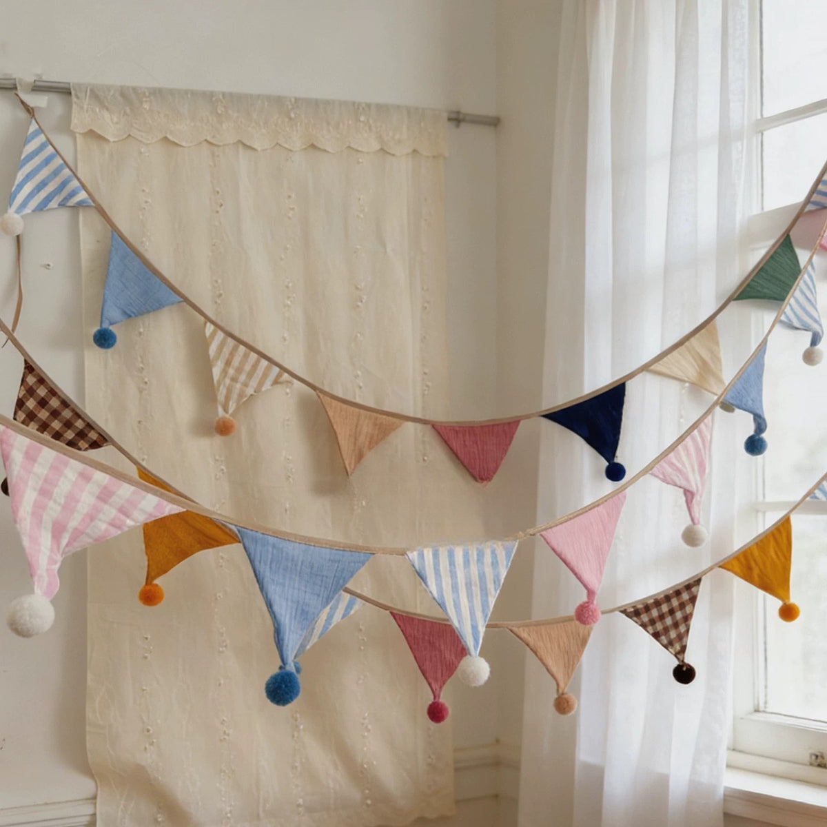 Two strings of pastel pom-pom bunting hanging in a sunny room