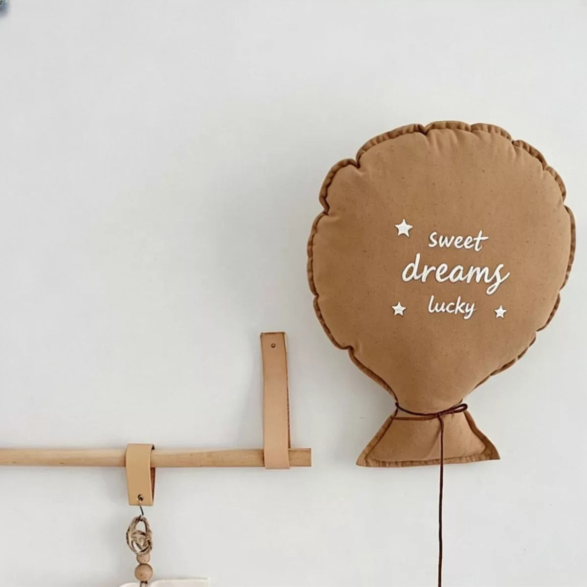Caramel balloon pillow embroidered "sweet dreams lucky" hanging on a nursery wall