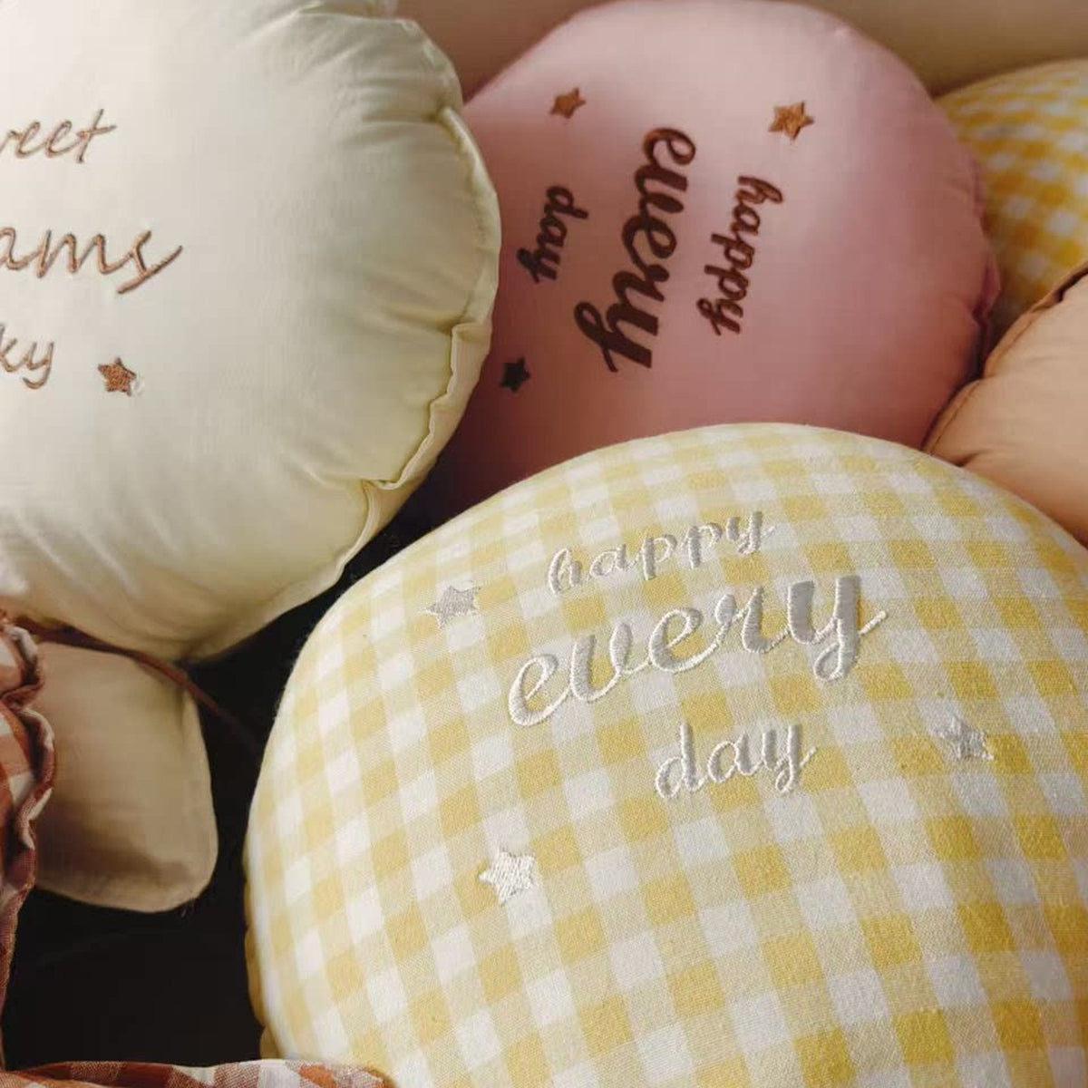 Close-up of embroidered balloon pillows in cream, pink and butter gingham