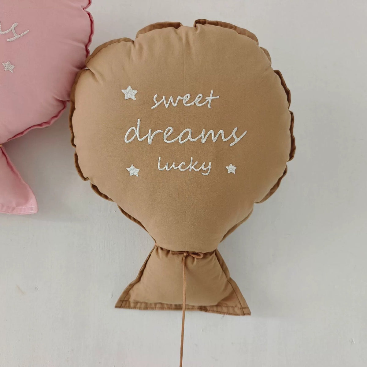Caramel balloon pillow embroidered "sweet dreams lucky" on a wall