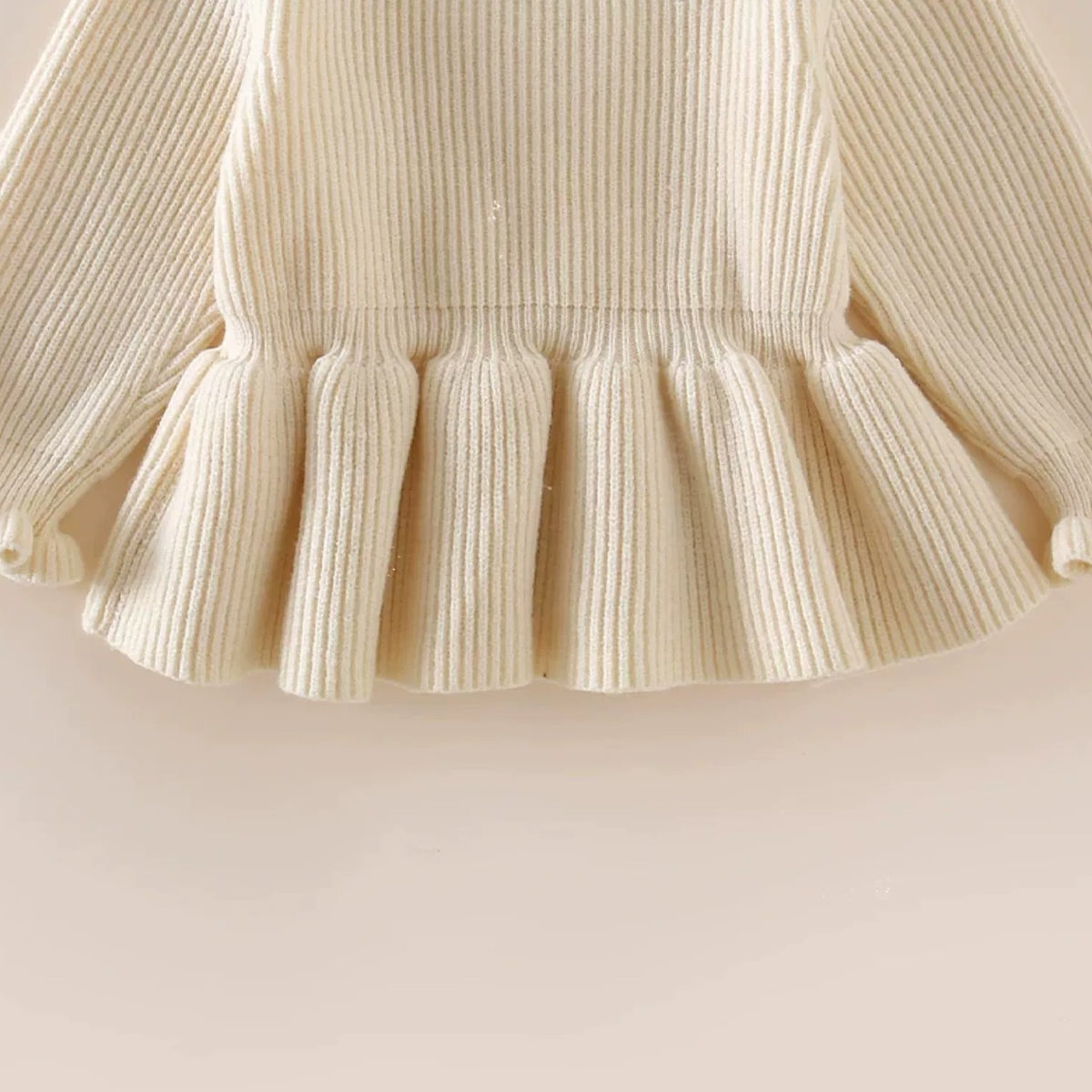 Close-up of the cream sweater's pleated peplum hem