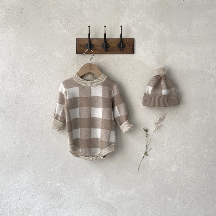Oat check knit romper hanging on a wooden hook rail