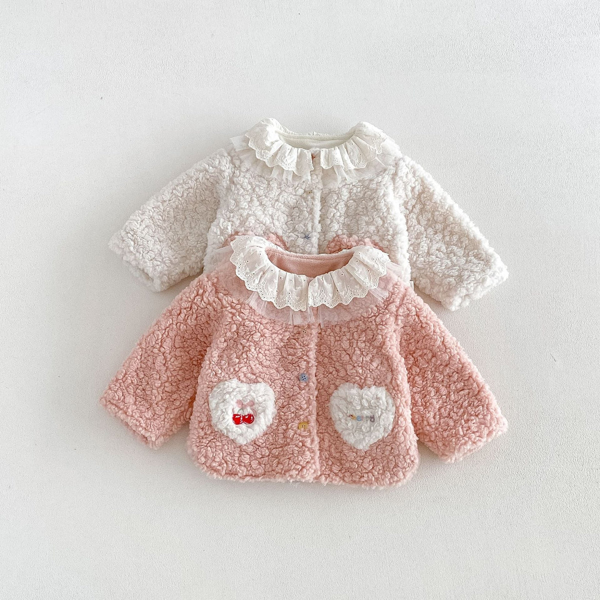 Pink and ivory girls fleece jackets layered on a white background