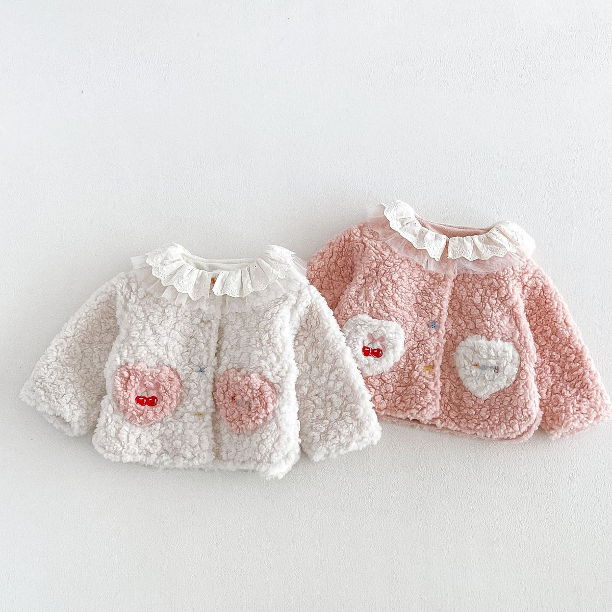 Ivory and pink sherpa jackets with lace ruffle collars and heart pockets, flat lay