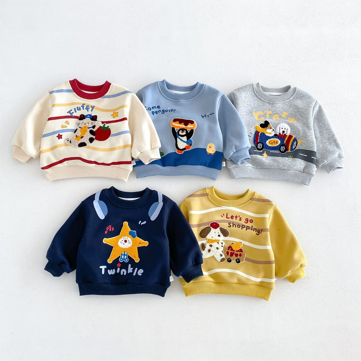 Five fleece-lined kids sweatshirts with embroidered animal patches, flat lay