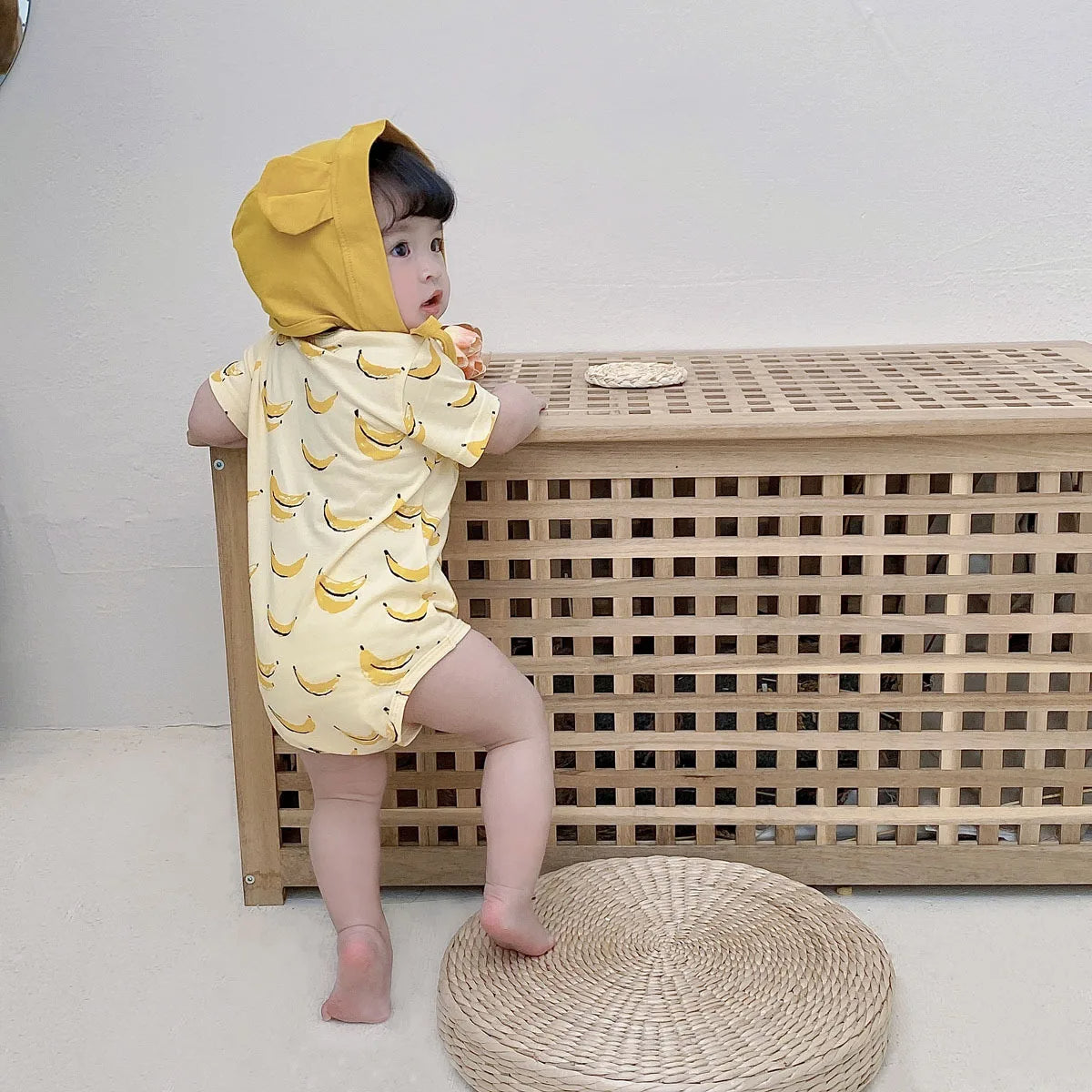 Baby in yellow banana print romper with hooded bear bonnet, back view