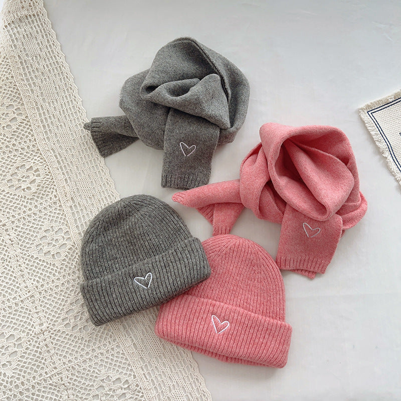 Charming winter accessory set featuring matching pink and gray knitted beanies and scarves, each adorned with a small embroidered heart detail. The beanies have a ribbed texture for warmth, while the scarves are soft and cozy, ideal for bundling up in colder weather. Displayed on a minimalist background with lace accents, this set combines style and comfort, perfect for showcasing in e-commerce listings or seasonal fashion catalogs.
