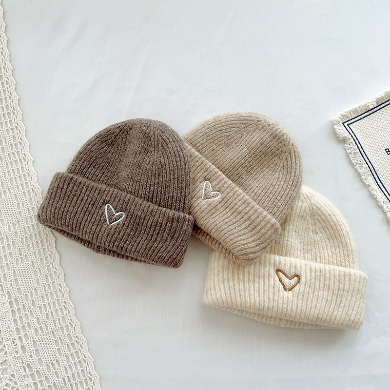 Set of three cozy knitted beanies in earthy neutral tones—brown, beige, and cream—each featuring a small embroidered heart on the cuff. These soft, warm hats are perfect for adding a touch of charm to a winter outfit. The subtle heart embroidery detail adds a playful yet stylish accent, making them suitable for both kids and adults.