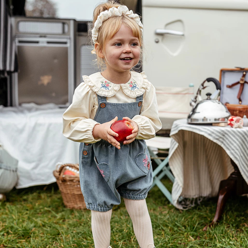Smiling girl holding an apple in denim blue strawberry shortalls