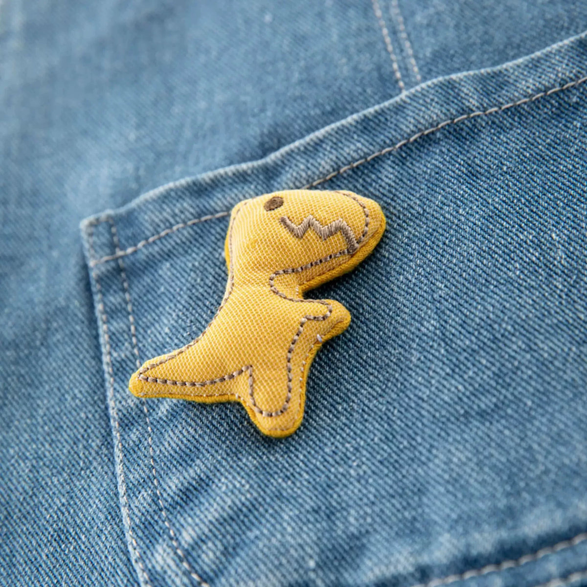 Close-up of the plush yellow dinosaur on the denim bib pocket