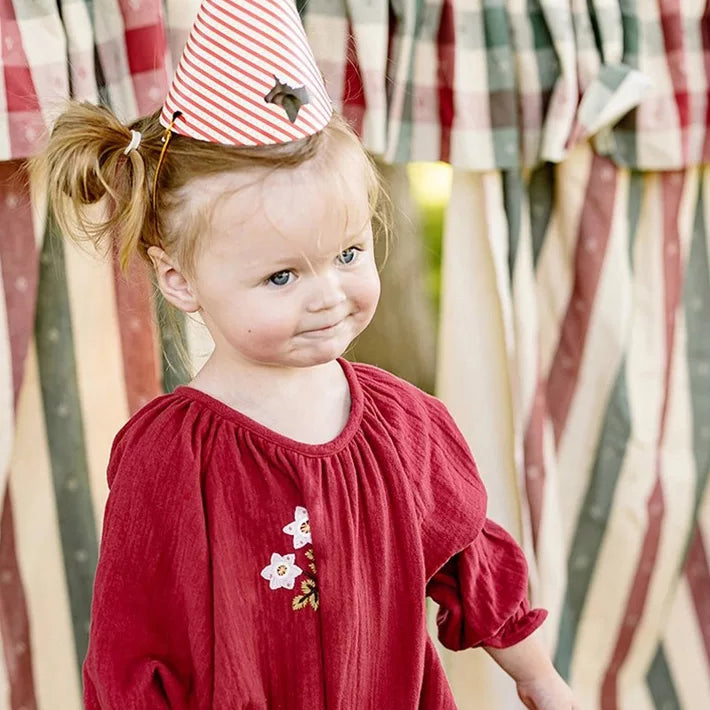 Little girl smiling in a brick red embroidered gauze bubble romper