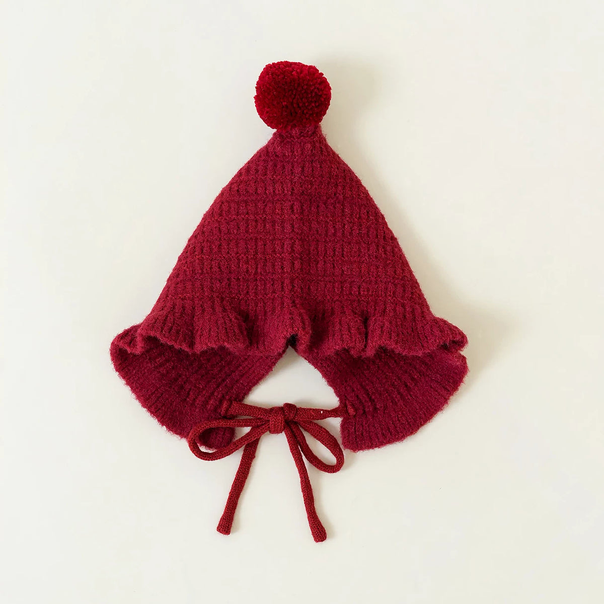 Berry red pointed knit baby hat with a single pom-pom on top, flat lay