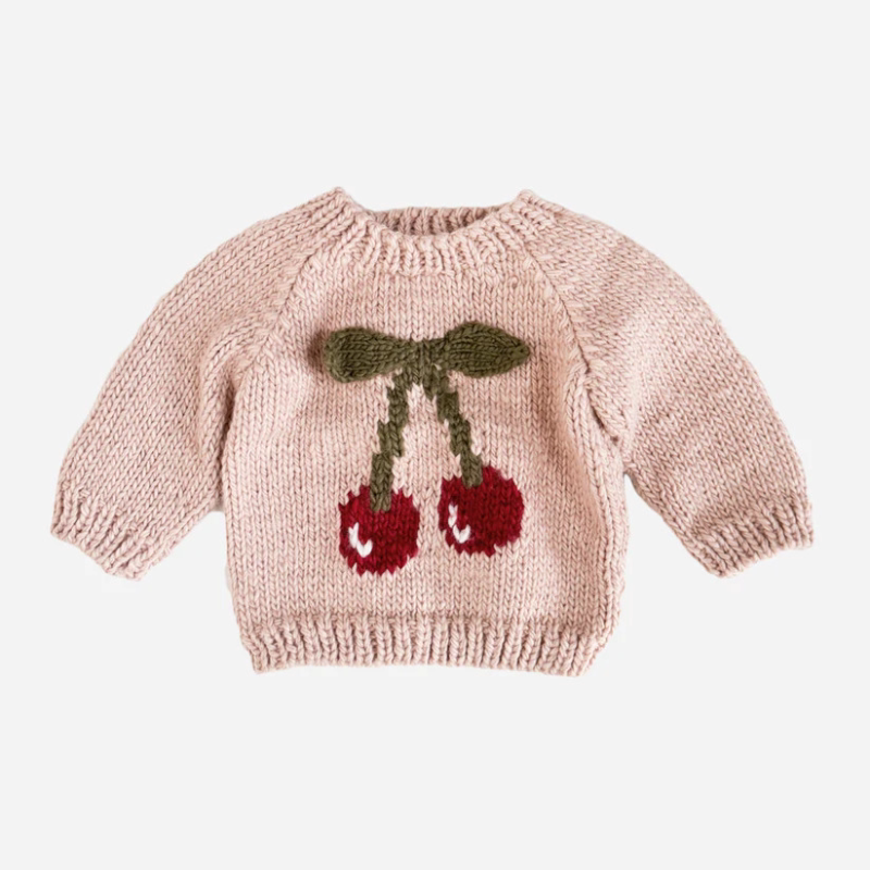Blush pink chunky knit kids sweater with a cherry motif, flat lay