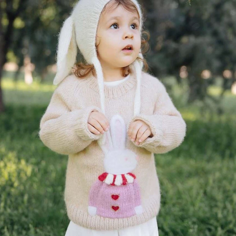 Toddler wearing a cream bunny sweater and a white bunny-ear bonnet