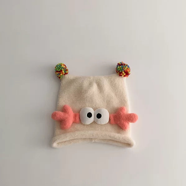 Cream knit baby beanie with coral antlers and googly eyes, flat lay