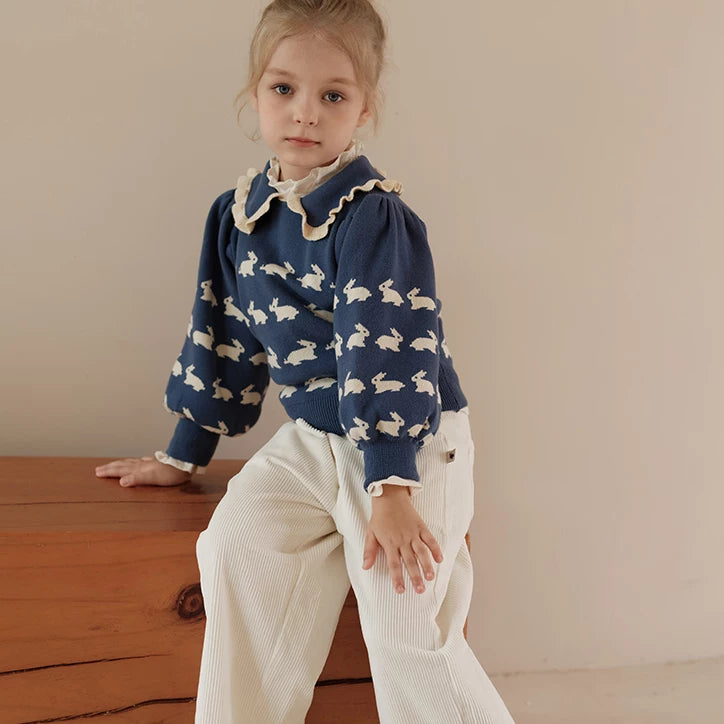 Girl sitting on a wooden bench in a navy bunny knit sweater