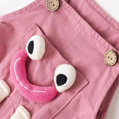 Wooden button strap and smiley pocket on pink overalls