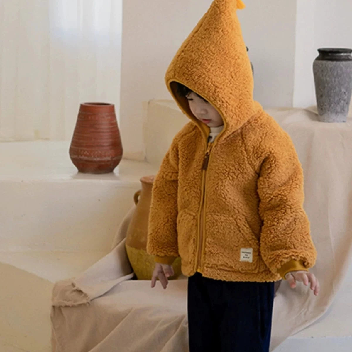 Child wearing a mustard teddy fleece jacket with the hood up