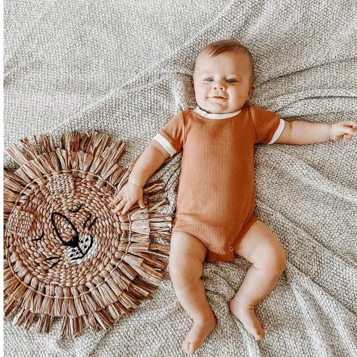 Baby lying next to a woven rug in a caramel short sleeve romper