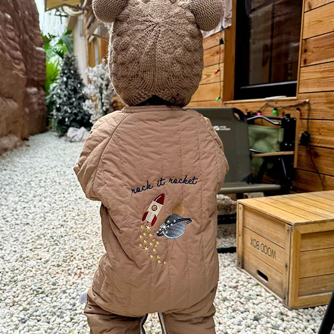 Back view of a toddler in a brown quilted romper with rocket embroidery