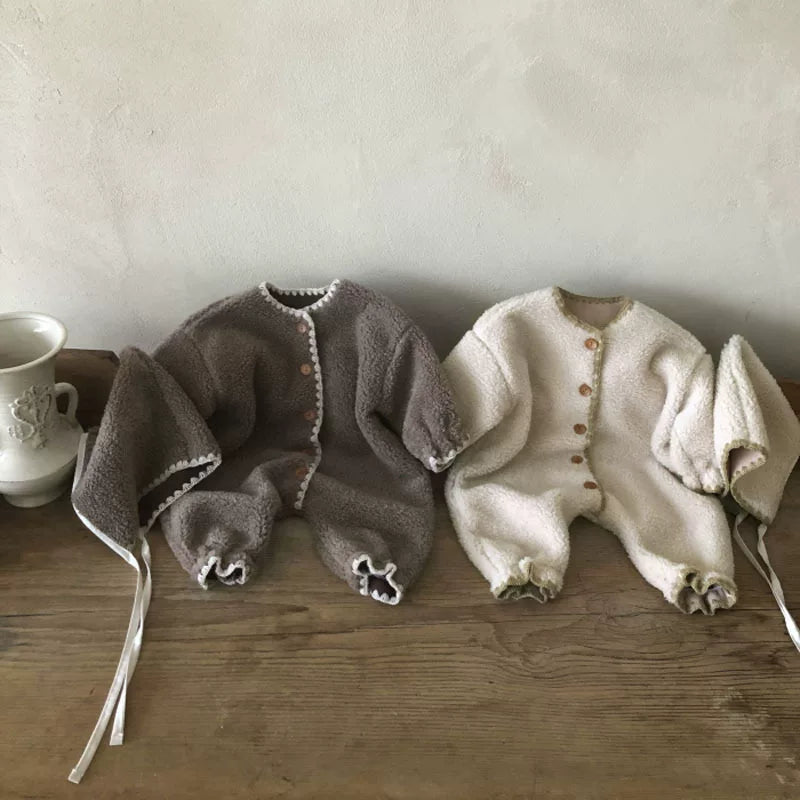Mocha and oat fleece baby rompers with gathered ankles on a wooden table