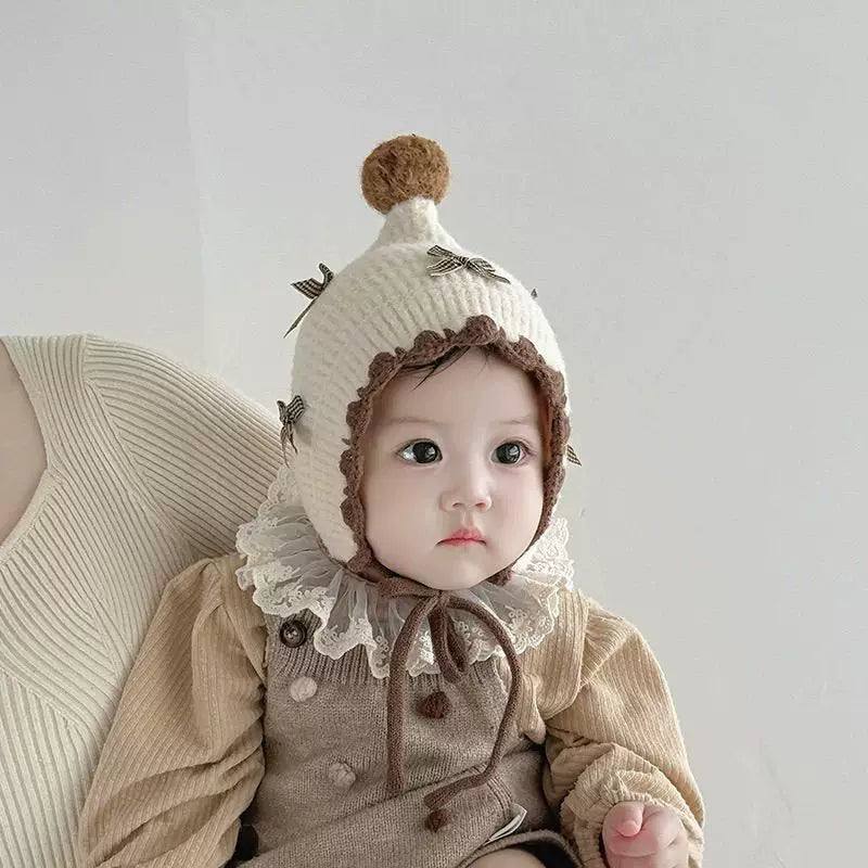 Baby girl in a cream knit pixie bonnet with bows and a pom-pom