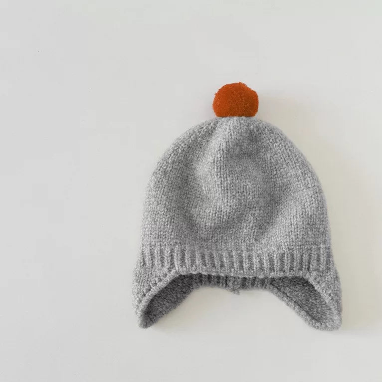 Dove grey knit baby earflap hat with orange pom-pom, flat lay
