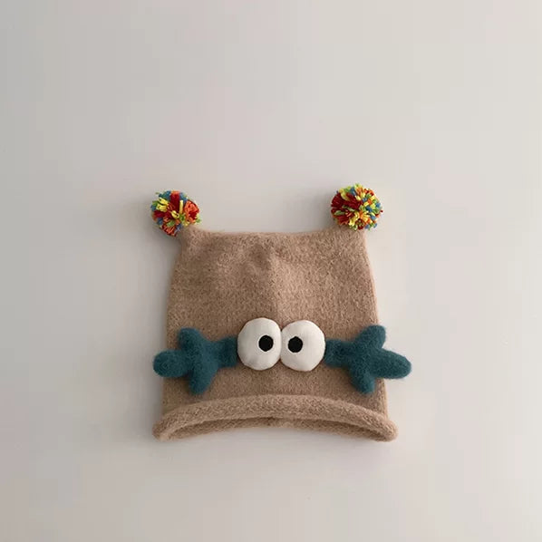 Oatmeal knit baby beanie with teal antlers and googly eyes, flat lay