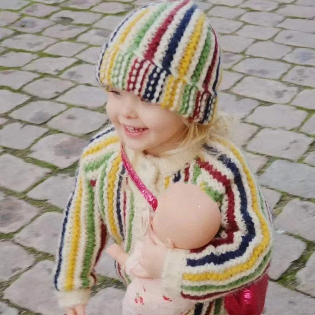 Toddler girl in a chunky rainbow stripe knit cardigan walking on cobblestones