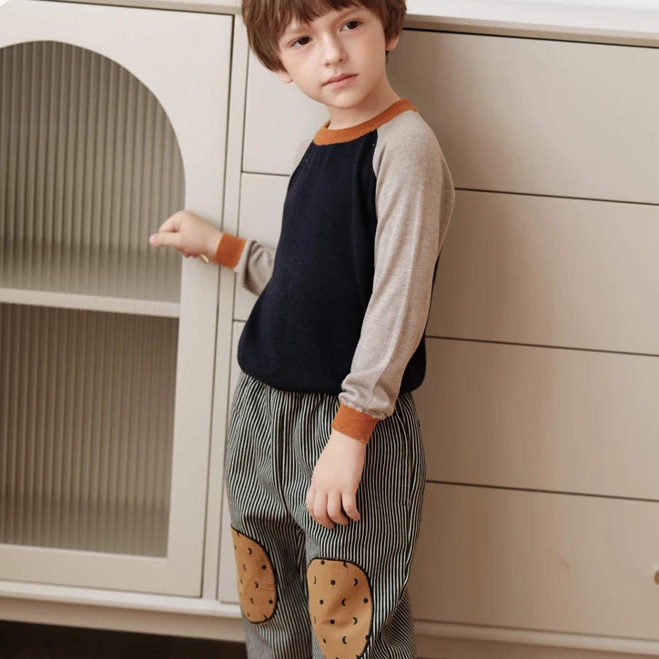 Boy standing by a window in charcoal striped warm trousers