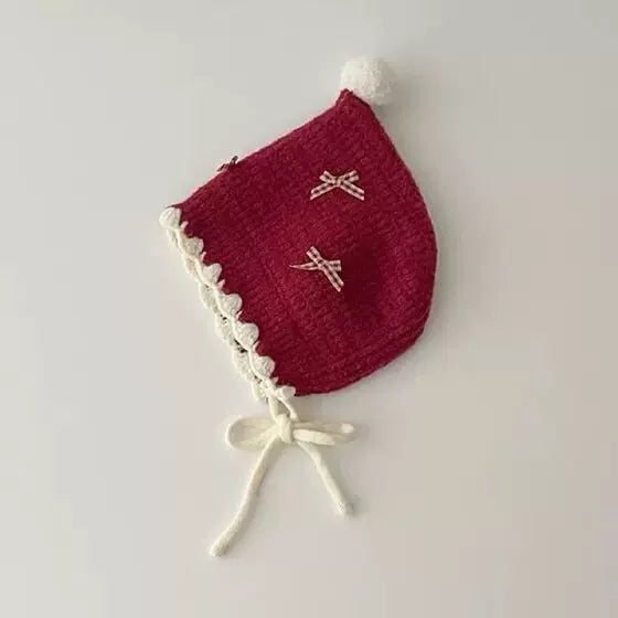 Berry red knit pixie bonnet with cream trim and ties, flat lay