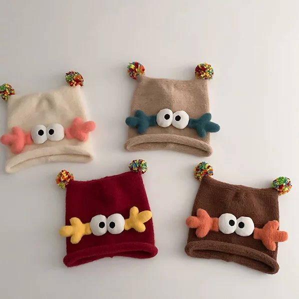 Four googly-eye knit beanies in cream, oatmeal, cherry red and cocoa, flat lay
