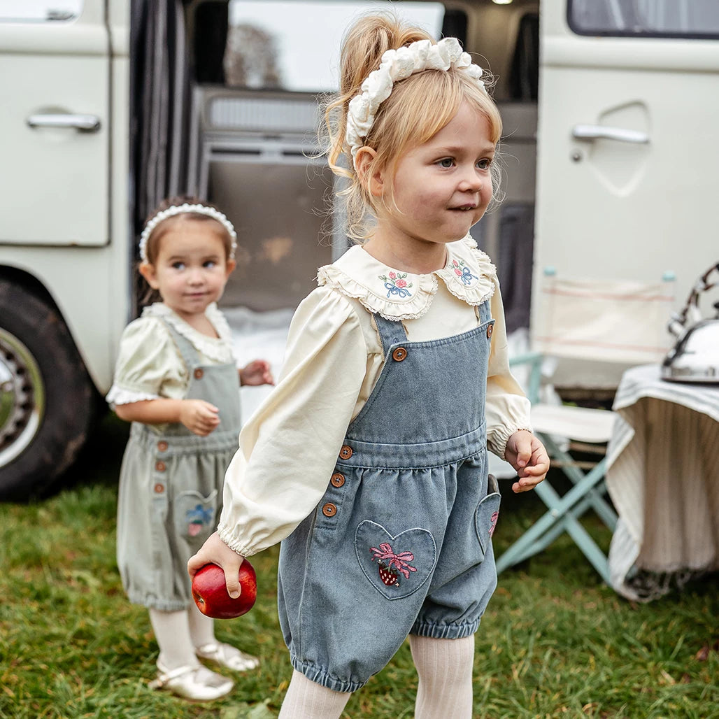 Two little girls in denim blue and sage strawberry shortalls