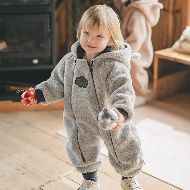 Toddler in a grey teddy fleece bear romper holding a bauble