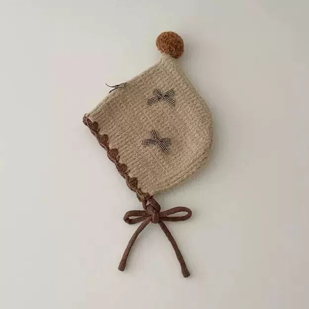 Oat knit pixie bonnet with little bows and brown ties, flat lay