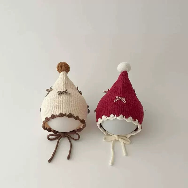 Cream and berry red pixie bonnets with pom-poms on display heads