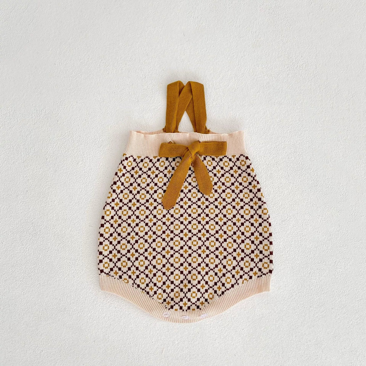 Knit suspender romper with caramel straps and bow, flat lay