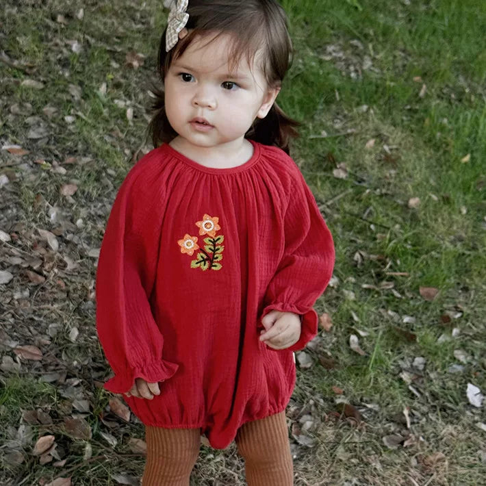 Baby girl standing on the grass in a red embroidered bubble romper