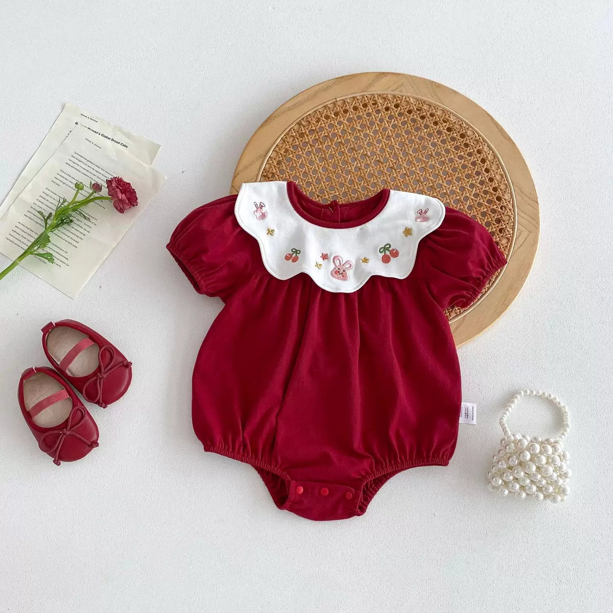 Red short-sleeve baby bodysuit with embroidered scalloped collar, styled flat lay