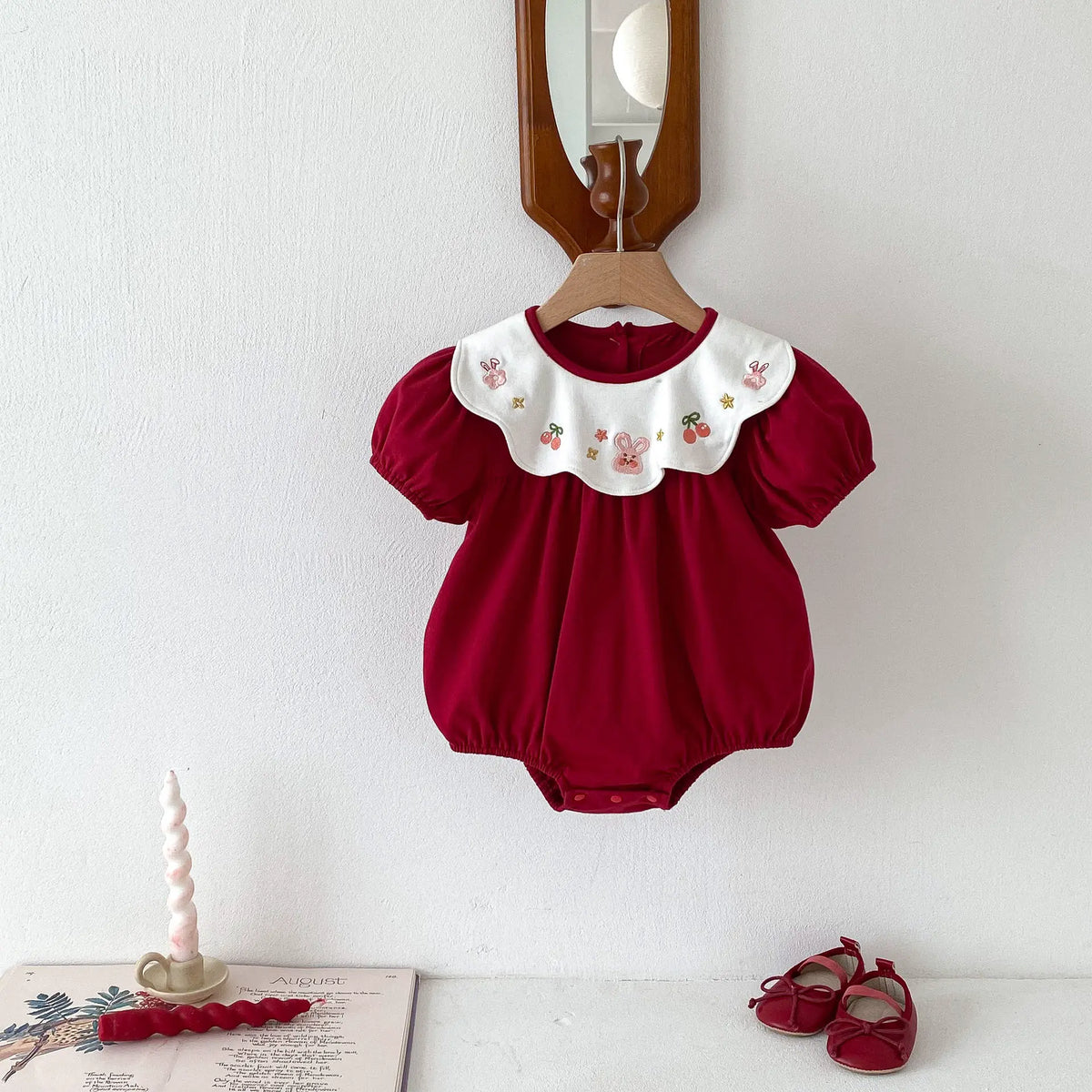 Red embroidered collar baby bodysuit hanging on a wooden hanger