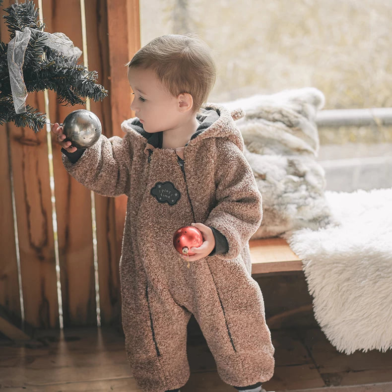 Little boy in a mocha fleece romper decorating a Christmas tree