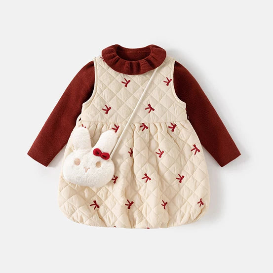 Three-piece girls dress set laid flat: cream quilted bow-embroidered pinafore over a burgundy ruffle-collar sweater with bunny bag
