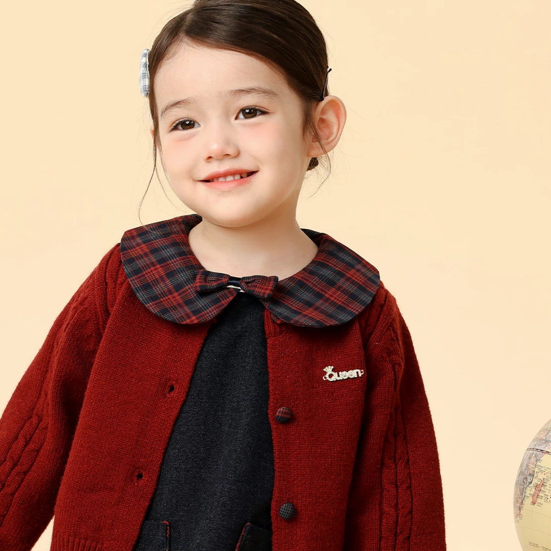 Girl wearing the plaid-collar navy dress and burgundy cardigan beside a vintage globe