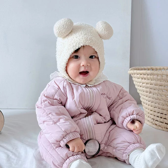 Smiling baby sitting in a pink quilted padded winter romper
