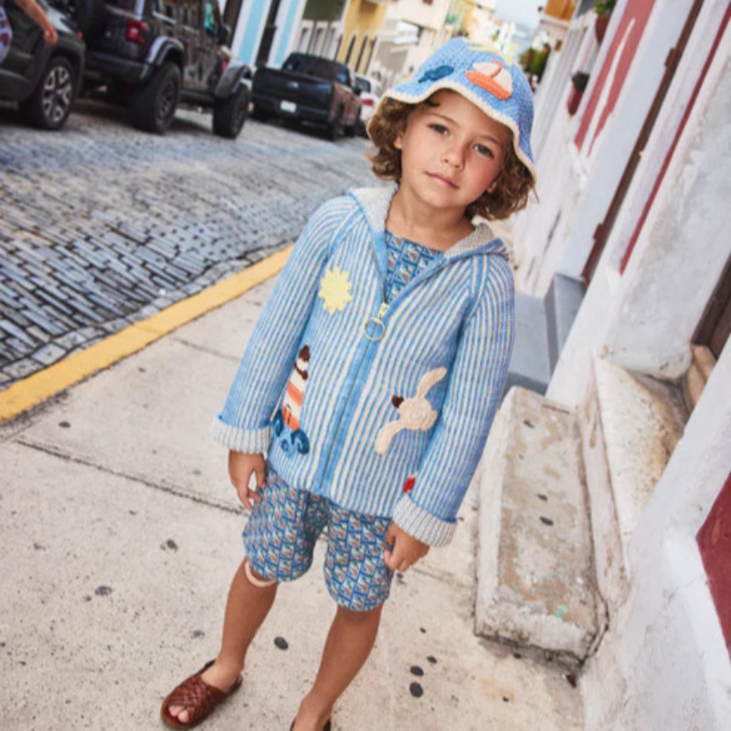 Child in a sky blue knit hoodie and bucket hat on a sunny street