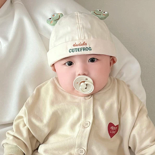 Baby with a pacifier in a cream frog beanie