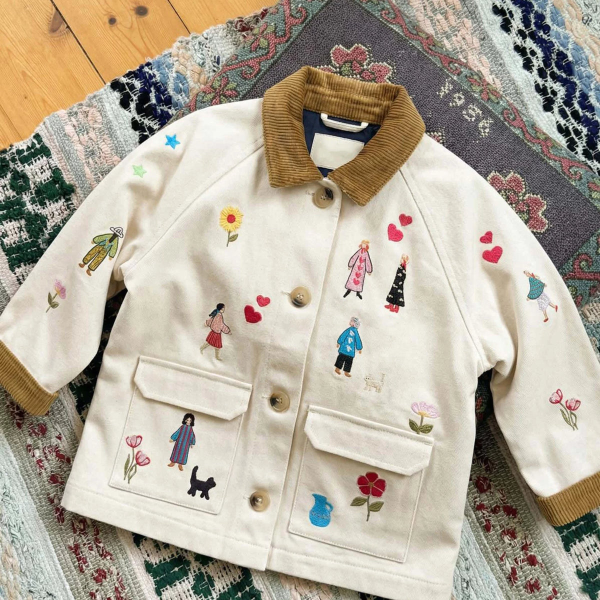 Embroidered cream kids jacket laid flat on a woven rug