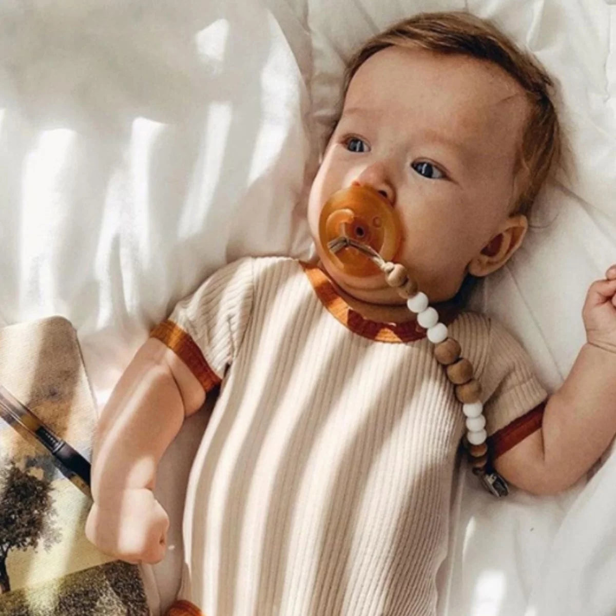 Baby with a pacifier wearing an apricot ribbed bodysuit with rust trim