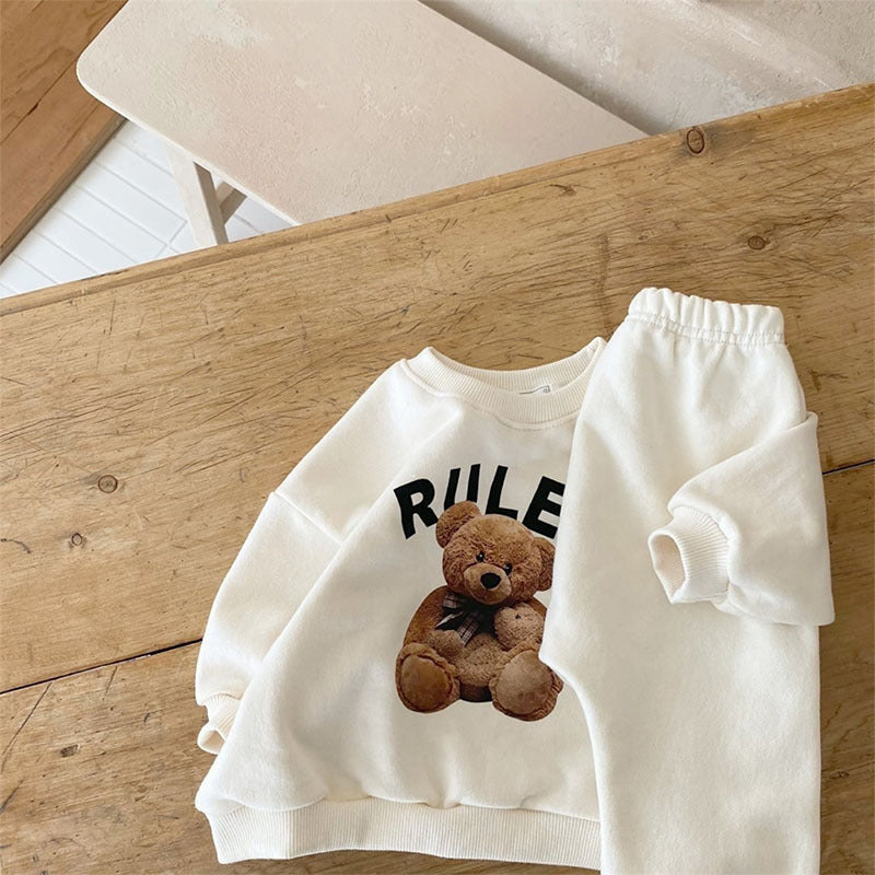 Teddy bear graphic sweatshirt and cream jogger pants on wood surface